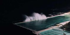 an empty swimming pool at night with the lights on and water spraying up from it