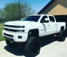 a white truck is parked in front of a house with black tires and rims