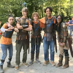 a group of people standing next to each other on a dirt road with trees in the background