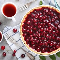 a pie with cherries on it sitting next to two cups of tea and silverware