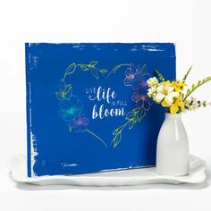 a vase filled with flowers next to a blue sign that says live life full bloom