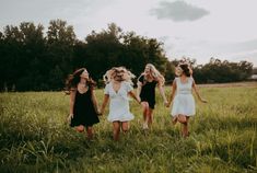 four girls in dresses are running through the grass with their hands in each other's pockets