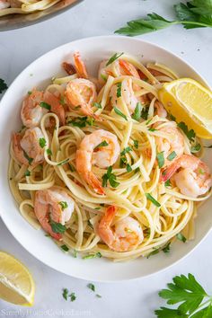 pasta with shrimp and parsley in a white bowl next to lemon wedges on the side