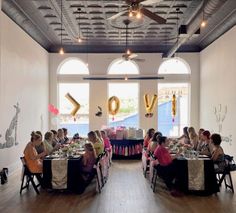 a group of people sitting at tables in a room with balloons and streamers on the ceiling