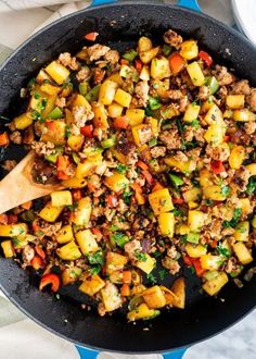 a skillet filled with meat and vegetables on top of a blue table cloth next to a wooden spoon