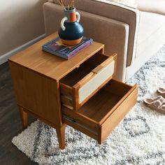 a wooden table with two drawers and a blue vase on top, in front of a couch