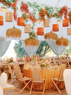 the tables are set up with orange and white flowers hanging from the ceiling above them