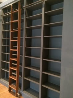 an empty bookcase with ladder leaning against the wall