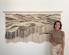 a woman standing in front of a wall hanging with fringes and beads on it