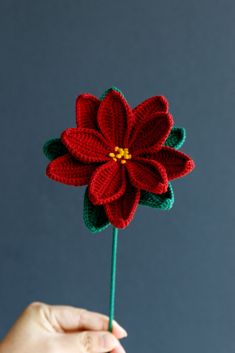 a crocheted red flower being held by a person's hand on a gray background