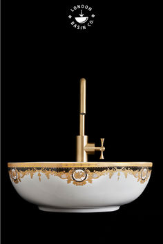 a white sink with gold trim and a faucet in the middle on a black background