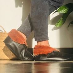 a woman's feet wearing black leather slippers with orange fur