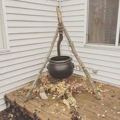 a pot sitting on top of a wooden platform in front of a house with brooms