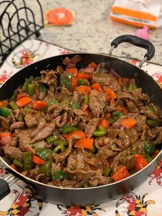 a pan filled with beef and peppers on top of a table next to utensils