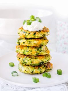 a stack of zucchini fritters topped with sour cream and green onions