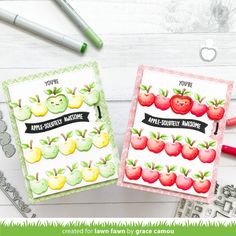 two cards with apples on them sitting next to some crayon markers and pencils