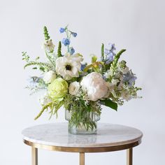 an arrangement of flowers in a glass vase on a marble table with a gold base