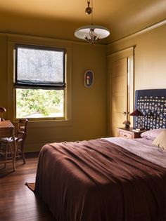 a bedroom with a bed, table and chair in it next to a large window