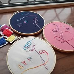 three embroidery hoops with different designs on them sitting on a wooden table next to some thread