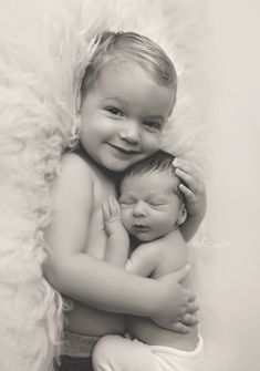 two babies are hugging each other on a fluffy white blanket in this black and white photo