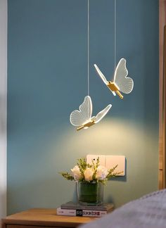 two white butterflies are suspended from the ceiling above a table with flowers and books on it