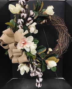 a wreath with white flowers and green leaves hanging from the front of a black wall