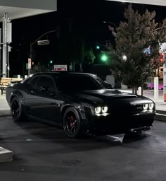 a black car is parked in front of a gas station at night with its lights on