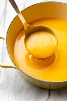 a ladle filled with orange liquid on top of a white marble countertop next to a wooden spoon