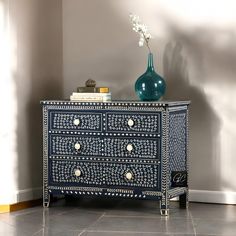 a blue and white chest of drawers in a room with a green vase on top