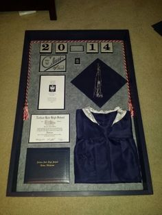 graduation decorations are displayed on the floor in front of a black framed display with diplomas, caps and tassels