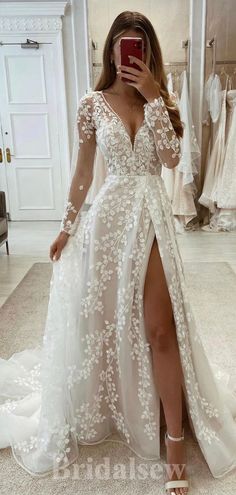 a woman taking a selfie while wearing a wedding dress with long sleeves and thigh high slit