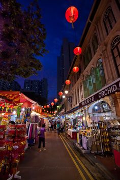 an outdoor market with red lanterns hanging from the ceiling and people shopping in the street