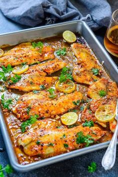 chicken with lemons and parsley in a baking pan next to a glass of beer