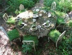 a table and chairs covered with moss in the woods