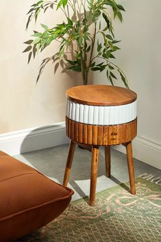 a wooden stool sitting next to a potted plant on top of a rug in front of a wall