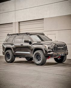 a large gray truck parked in front of a garage door next to a tall building