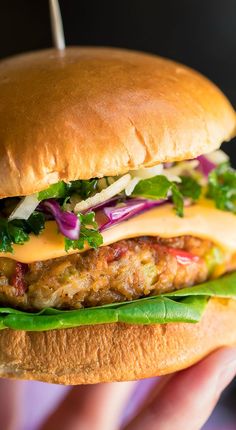 a hand holding a hamburger with lettuce, cheese and other toppings on it