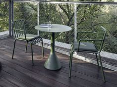 two green chairs and a table on a deck with trees in the backround