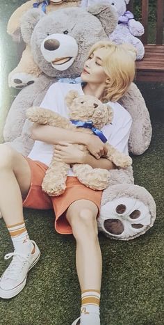 a woman sitting on the grass with two large teddy bears