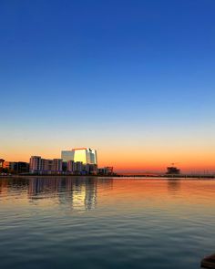 a body of water that has some buildings in the background and blue sky above it