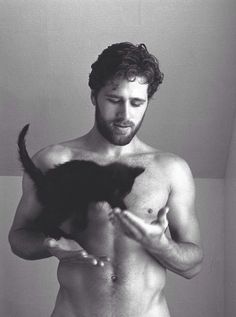 a shirtless man holding a cat in his hands