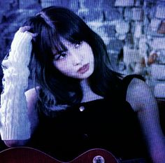 a woman holding a guitar in front of a brick wall with her hand on her head