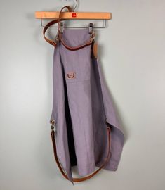 a purple apron hanging on a wall with a wooden hanger and two leather straps