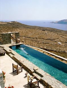 an outdoor swimming pool surrounded by stone walls and patio furniture with ocean in the background