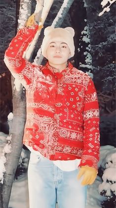 a young boy standing in front of a tree wearing a red shirt and white hat