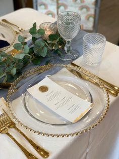 a table set with place settings, silverware and greenery for an elegant dinner