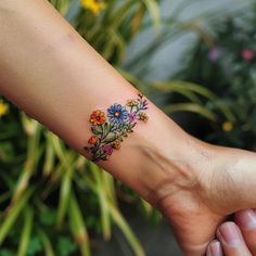 Wildflower Tattoo Design Set Around The Wrist Tattoos For Women, Wild Flower Wreath Tattoo, Botanical Wrist Tattoo, Small Floral Tattoo Designs For Women, Field Of Flowers Tattoo, Small Wildflower Tattoo Color, Grow Through It Tattoo, Wildflower Wrist Tattoo, Romantic Tattoos For Women