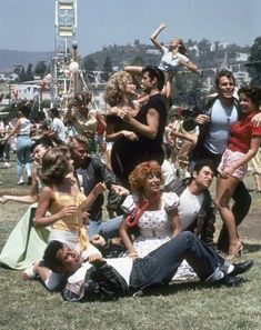 a group of people sitting and standing around each other in the grass at a music festival