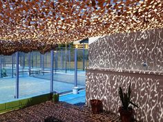 an indoor tennis court with many plants in the foreground and large windows above it