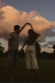 two people standing in the grass with their arms around each other and one person reaching for something